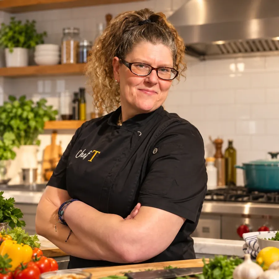 Chef Teey in her kitchen, surrounded by fresh vegetables and herbs